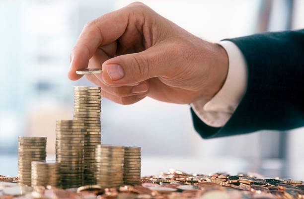 Hand of a mid adult man, wearing a suit, is stacking Euro coins.